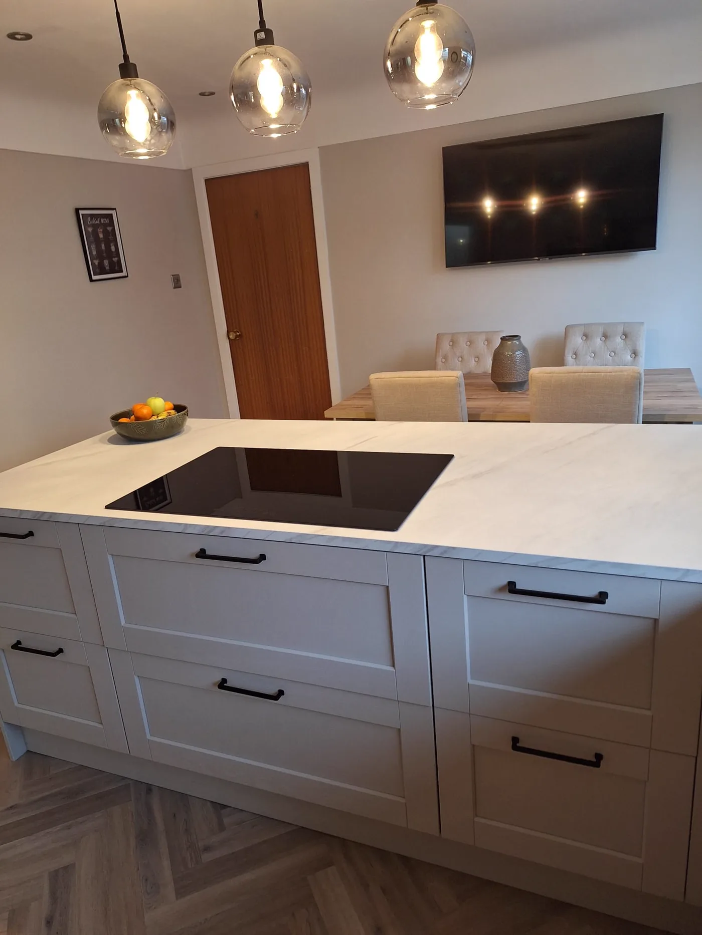 The finished kitchen, with a central island and black hob, pendant lights above and the living area beyond.