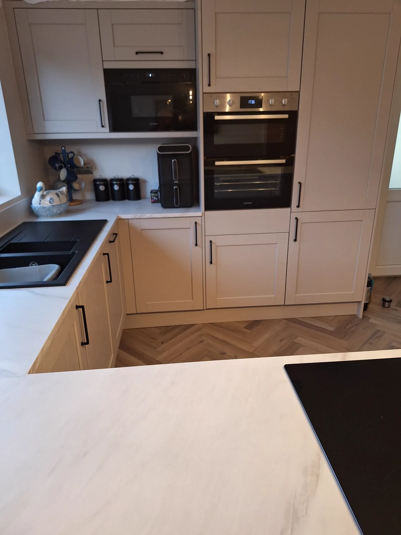 Tall units in the finished kitchen housing a black built-in microwave and double oven, with the herringbone floor alongside.