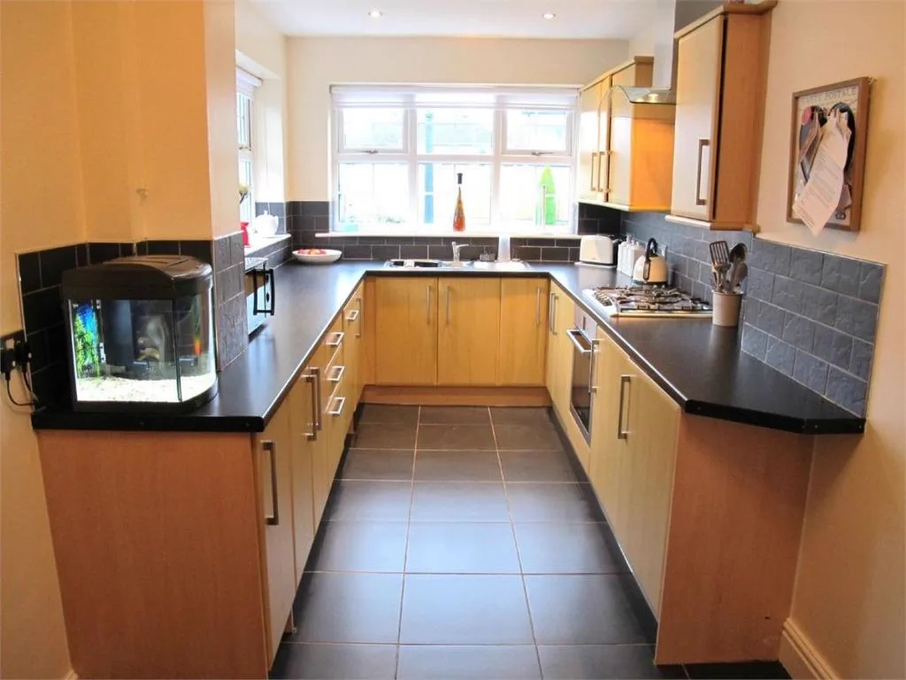 The original narrow kitchen, with orange-toned wood cabinets, black worktops and a tiled floor.